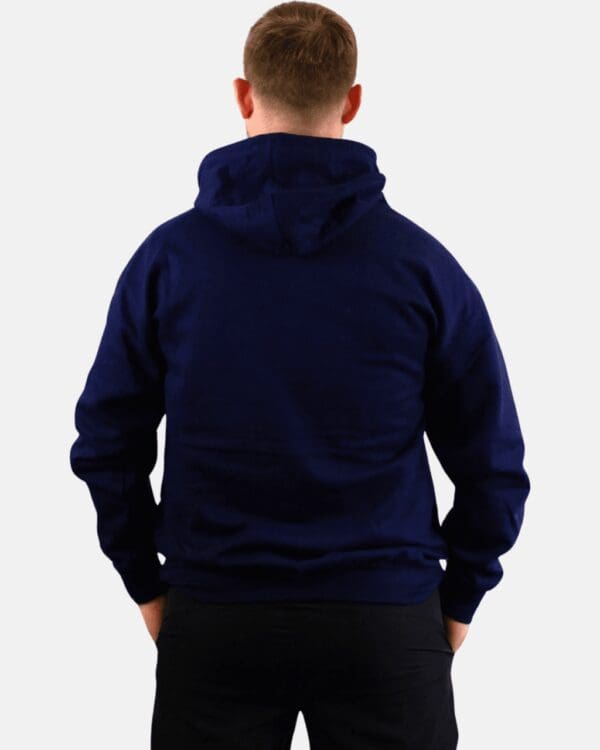 A man in a blue hoodie is standing with his hands on the back of his pockets.