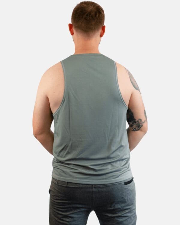 A man wearing a gray tank top with his hands on the back of his shirt.