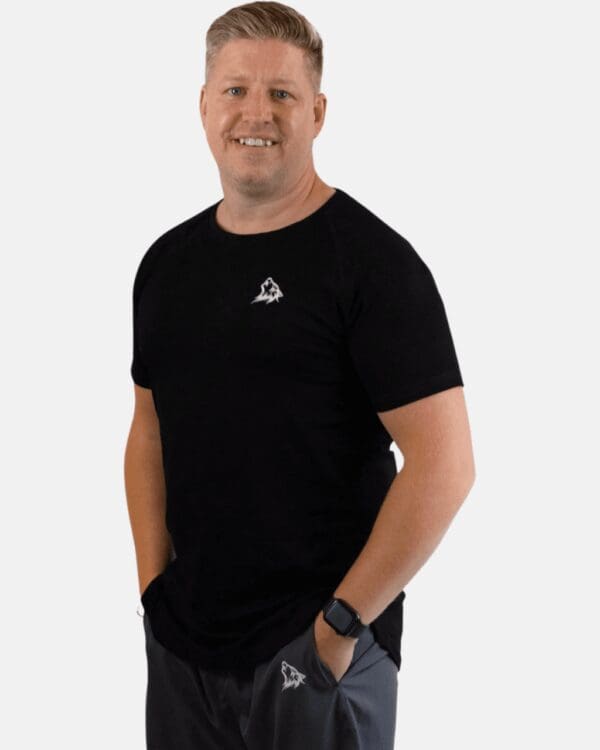 A man in black shirt standing next to a white wall.