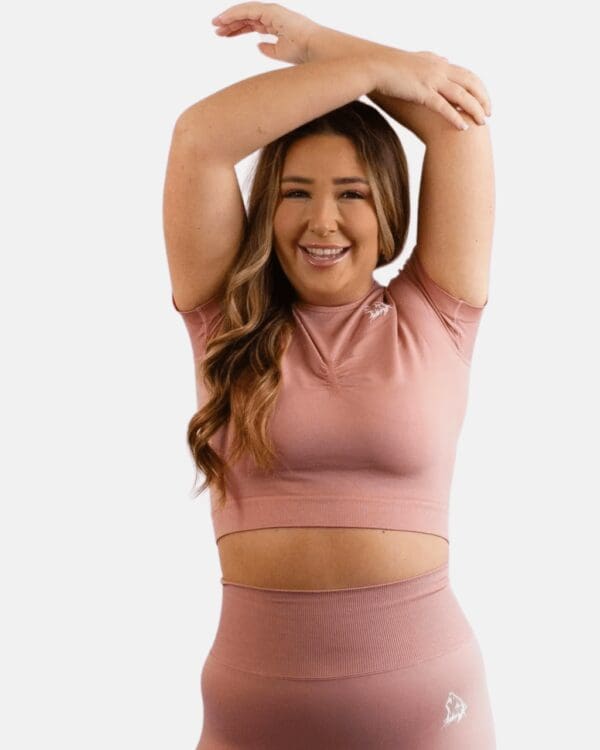 A woman in pink top and pants holding her hands up.