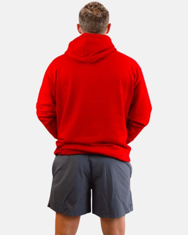 A man in red hoodie and shorts standing with his hands on the back of his hips.