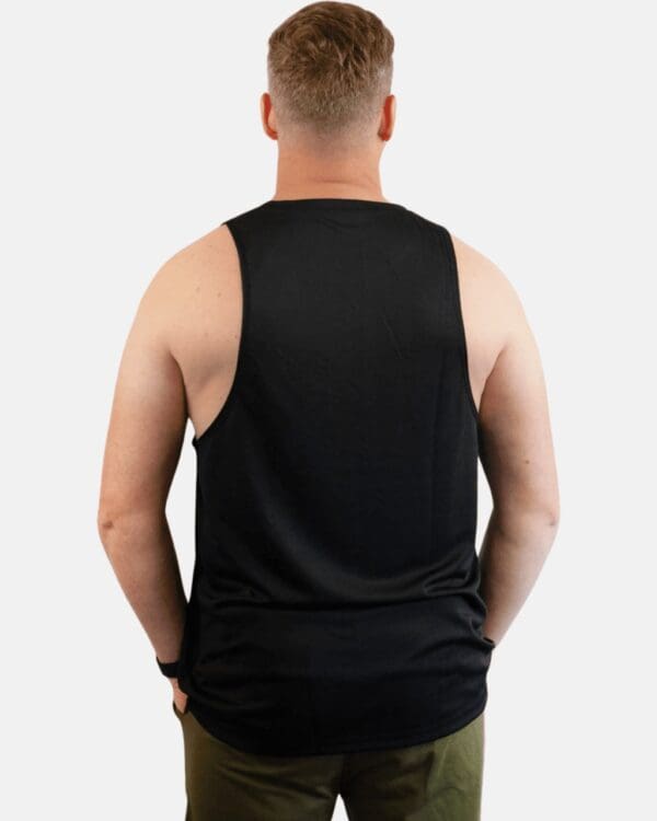 A man wearing black tank top with his hands on the back of his pants.