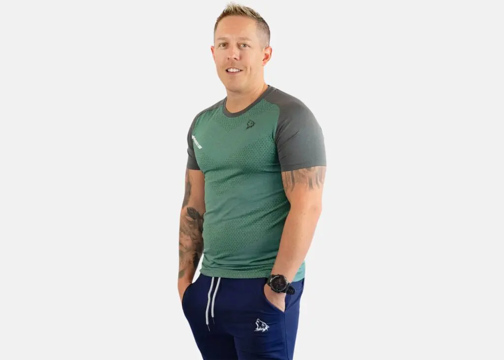 A man standing in front of the camera wearing blue pants and green shorts.